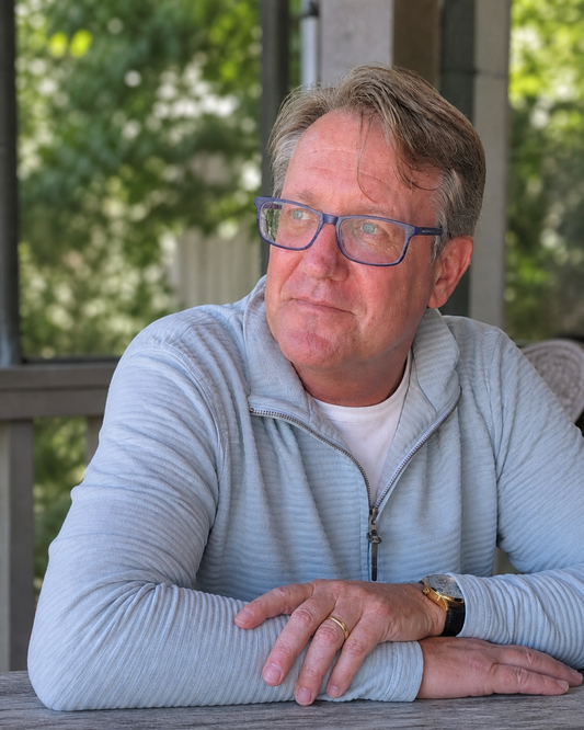A veteran sits quietly at a table, head bowed slightly — representing the invisible neurological toll of years of repetitive blast exposure in Special Forces service.