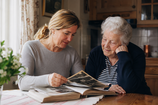 Adult daughter and elderly mother looking through a photo album together at a kitchen table